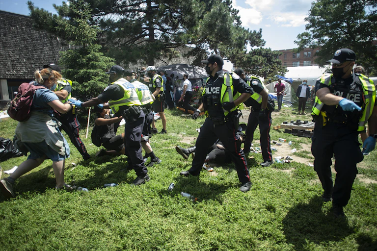 Police struggle with protesters as they clear a homeless encampment.