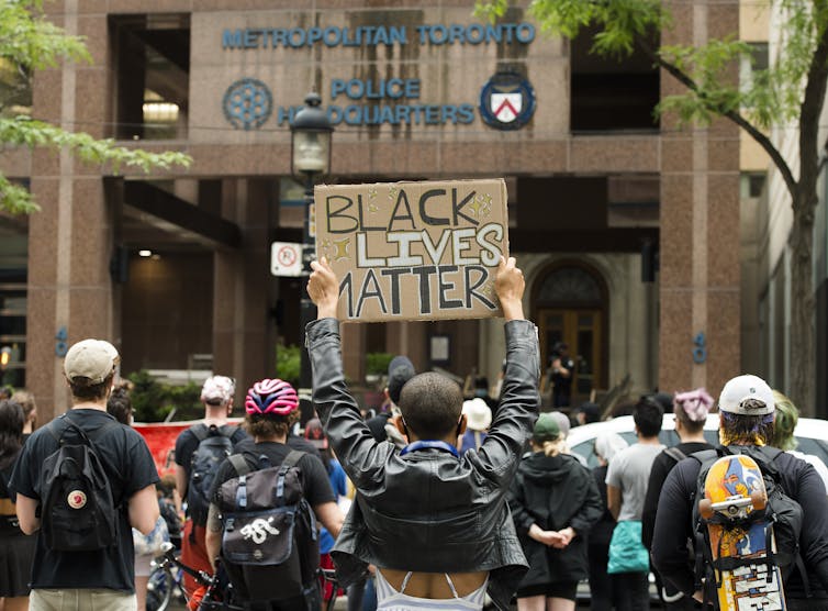 A crowd of people hold up Black Lives Matter signs in front of Toronto police headquarters.