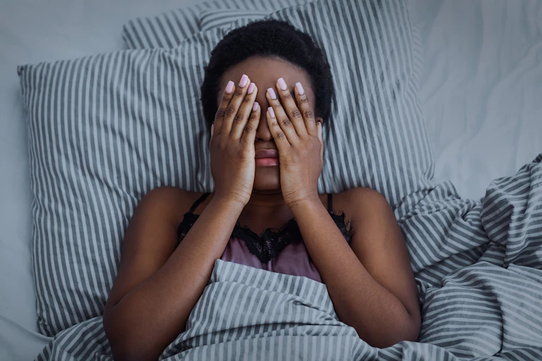 A woman lying in bed with her hands over her face.