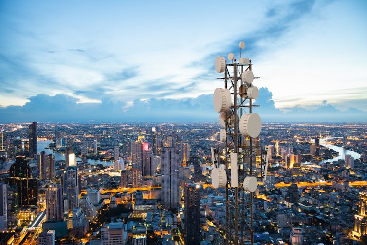 Telecommunication tower with 5G cellular network antenna on city skyline background.