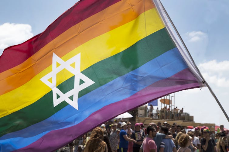 A rainbow pride flag with a white Star of David in the centre.