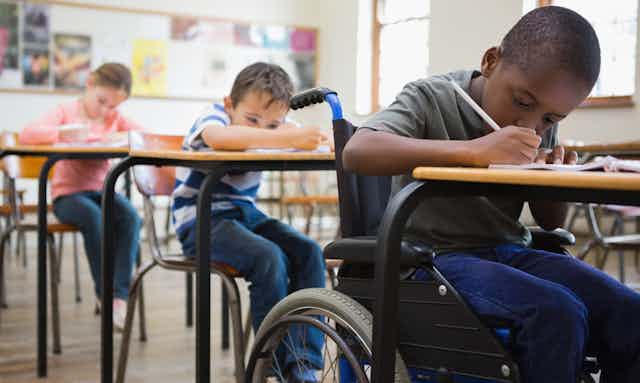 Students seen sitting in a classroom, one who is a wheelchair user.