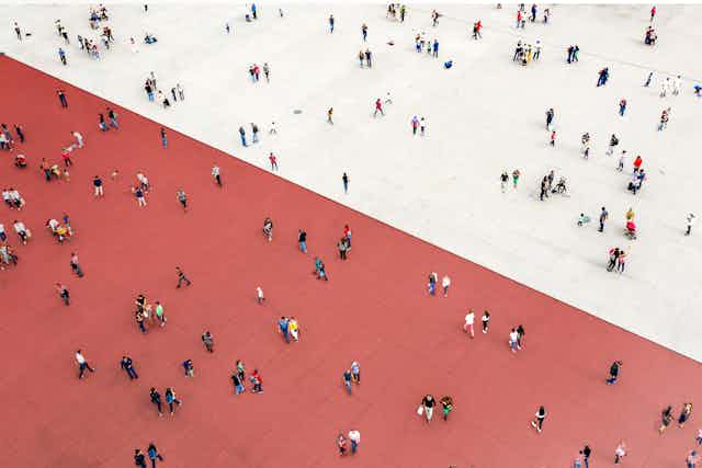 Many people are seen scattered across a large expanse of floor, some on a red side and some on a white side.