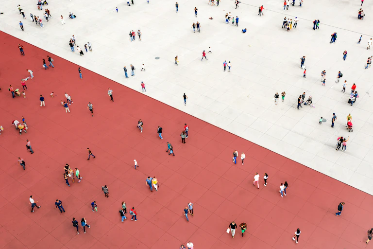 Many people are seen scattered across a large expanse of floor, some on a red side and some on a white side.