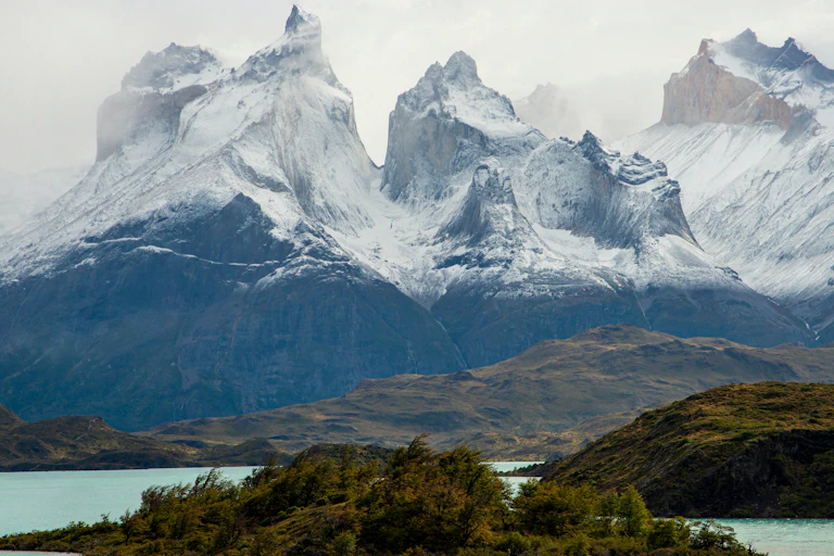 A mountainous landscape with green vegetation in the foreground and snowcapped mountains behind.
