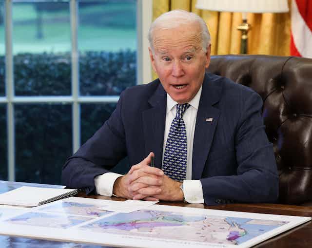 Joe Biden sits at his desk with his hands clasped.