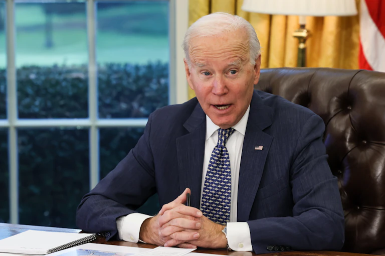 Joe Biden sits at his desk with his hands clasped.