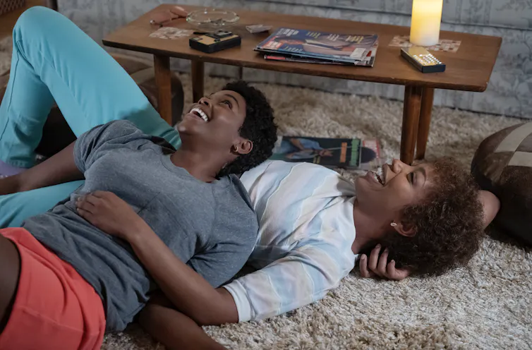 Whitey and Robyn lie together laughing on the floor of an apartment, embracing.