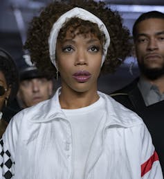 Naomi Ackie as Whitney Houston, wearing a white track top and matching hairband pushing her curly hair back from her face.
