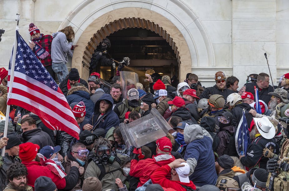 Dozens of people are crammed closely together in front of an arched opening in a marble building. Some hold American flags.