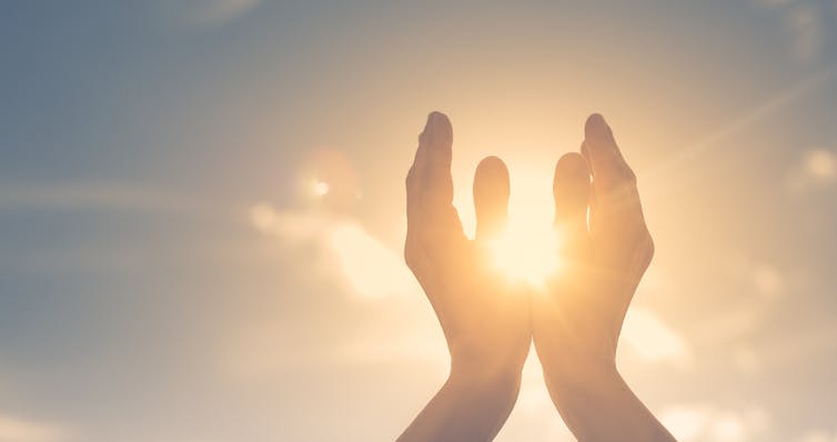 Photo of a pair of hands reaching up to the sky, cupped around the sun