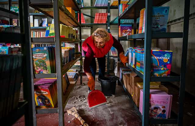 A woman uses a red dustpan to clean debris in a school in Ukraine that had been struck by a missile.