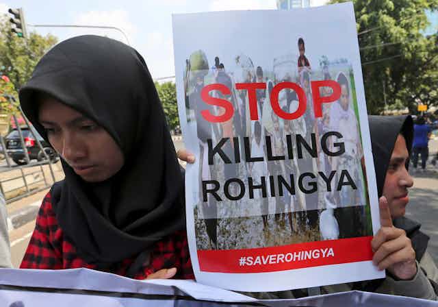 Two women wearing headscarves carry a sign that reads: Stop killing Rohingya.