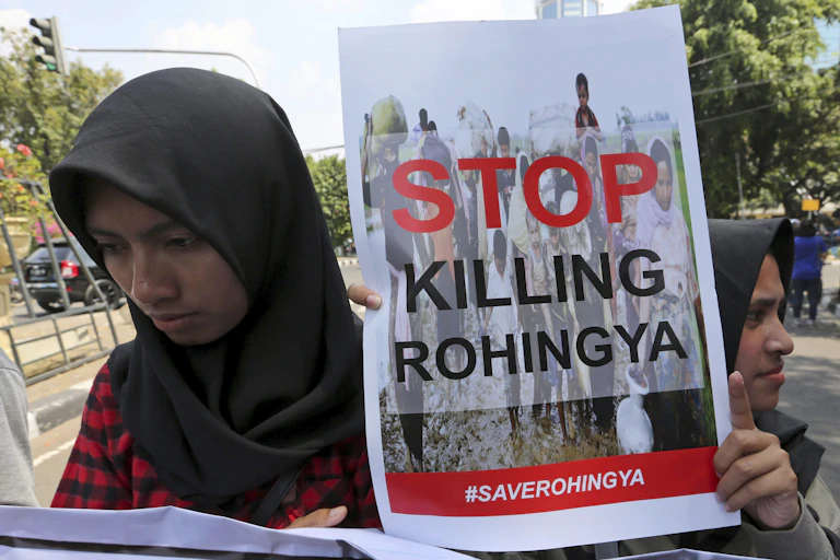Two women wearing headscarves carry a sign that reads: Stop killing Rohingya.