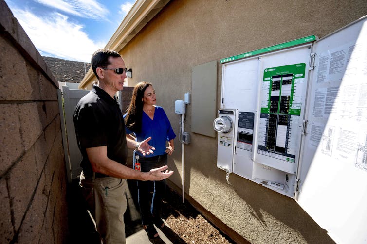 A man and woman stand beside a power box on a home.