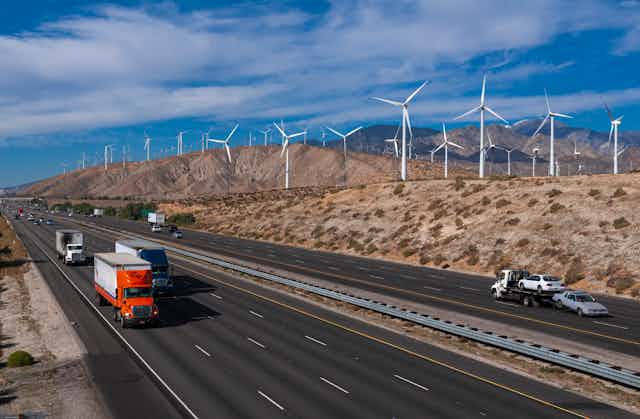 Trucks on a highway with wind turbines on the hills behind