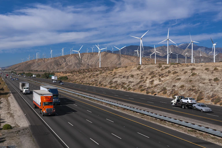 Trucks on a highway with wind turbines on the hills behind