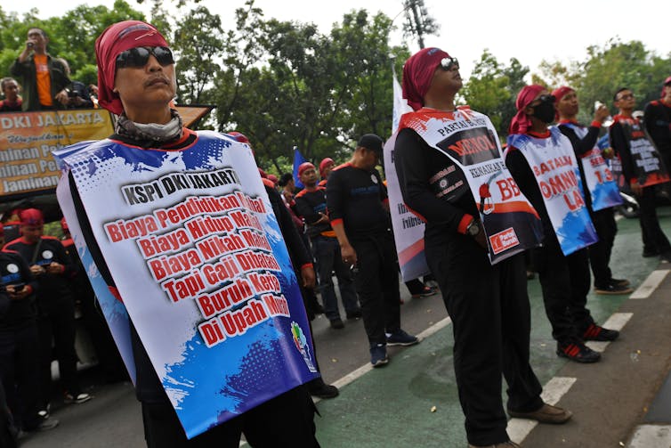 Protestors stand in a line wearing red bandanas and protest signs.