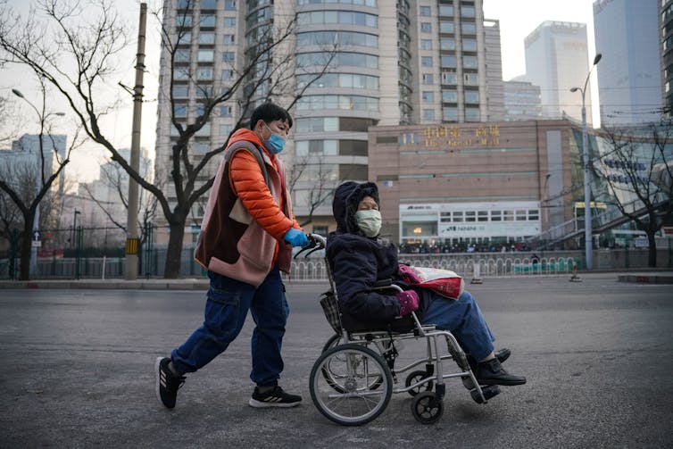 A woman pushes another woman in a wheelchair in Beijing.