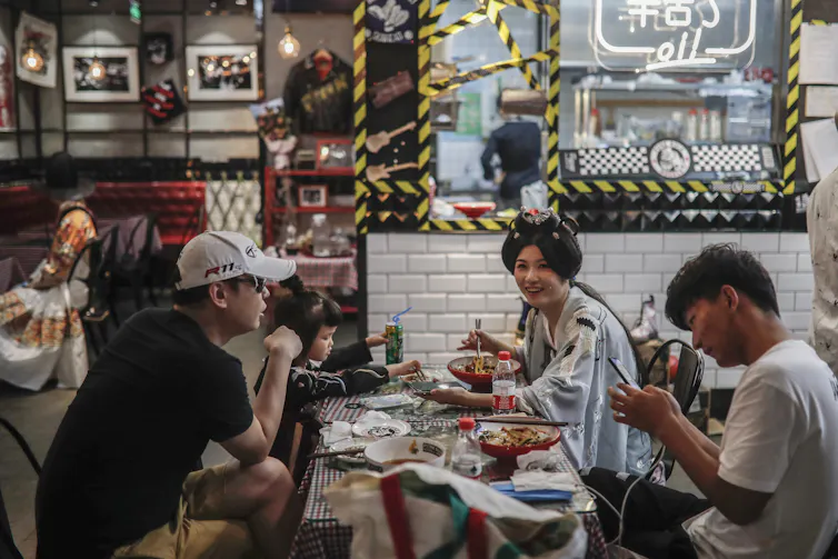 Young Chinese people sitting at a restaurant table, one is wearing traditional Chinese _hanfu_ clothing.