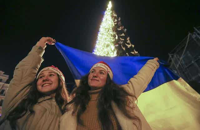 Two women wave a Ukraine flag in front of a Christmas tree in Kyiv.