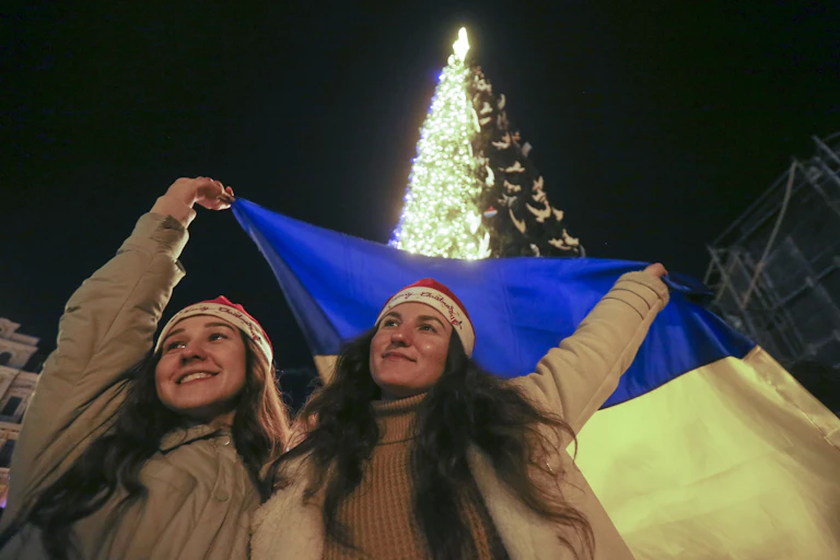 Two women wave a Ukraine flag in front of a Christmas tree in Kyiv.