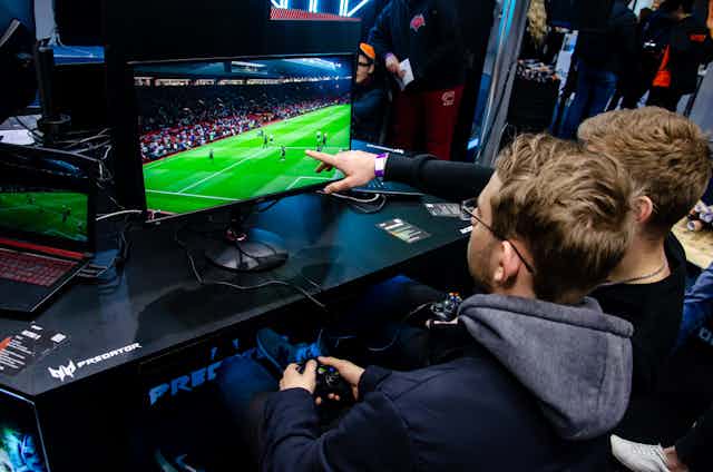 Two boys in front of a football videogame on a big screen.