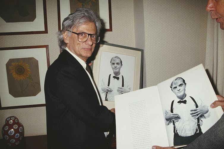 Man wearing glasses holds a portrait of a man wearing suspenders.