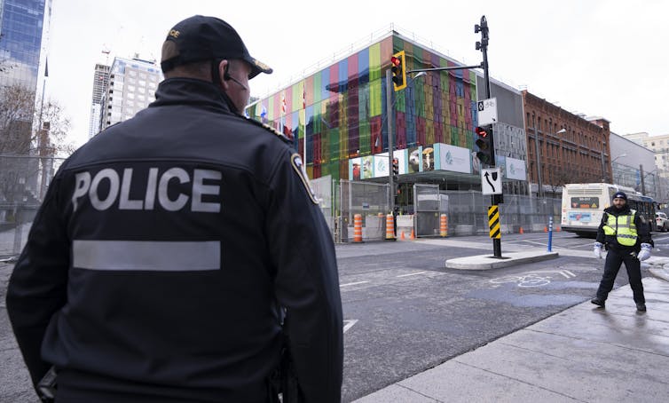 A police officer is seen from behind outside a convention centre. Police is written on the back of his jacket.