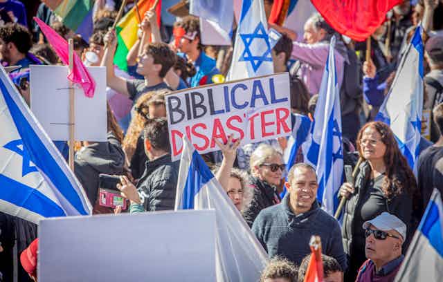 A group of protestors carrying Israeli flags and a sign that says 'BIBLICAL DISASTER'