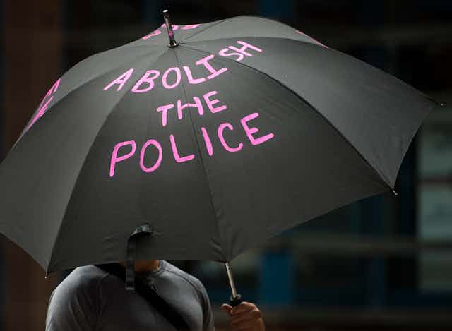 A black umbrella is emblazoned with the message Abolish the Police in bright pink lettering.