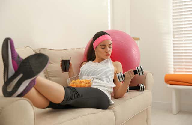Lazy young woman with sport equipment and junk food at home.