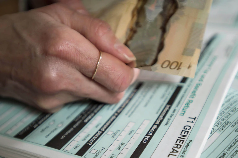 A woman's hand is seen holding a $100 dollar bill and over top a tax return.
