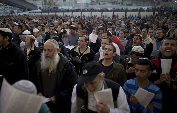 A large group of men standing in rows concentrate in prayer.