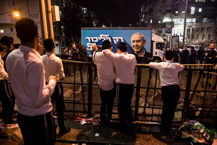 Teenage boys in white shirts and black slacks look at a political poster.