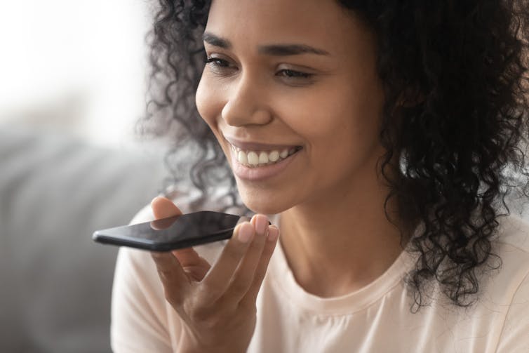 A smiling woman holds her smartphone up to her mouth to speak to a digital assistant