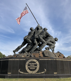 A statue shows a group of soldiers pushing a flag pole to erect the USA flag.