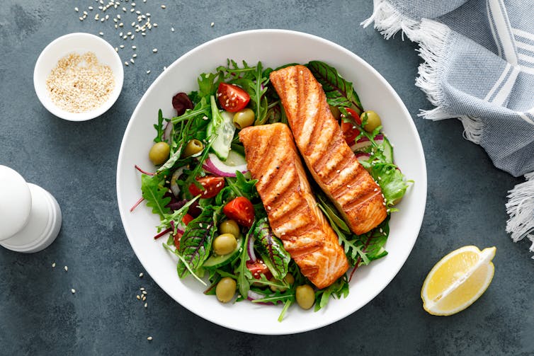 A bowl of greens with a two pieces of grilled salmon on top.