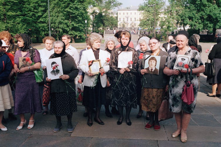Women standing in a row holding photographs.