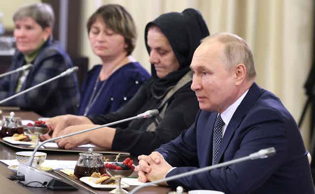 Women sitting in front of microphones next to President Putin.