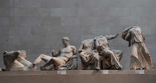Three statues from the Parthenon Marbles collection show a man reclining, two headless seated women and a standing headless figure.