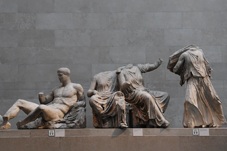 Three statues from the Parthenon Marbles collection show a man reclining, two headless seated women and a standing headless figure.