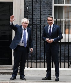 Social distancing, the two politicians wear blue navy suits. Mitsotakis is buttoned up while Boris's hangs open to reveal an unruly tie.