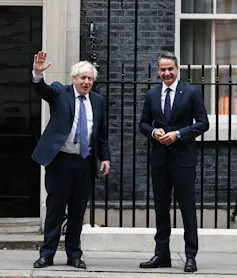 Social distancing, the two politicians wear blue navy suits. Mitsotakis is buttoned up while Boris's hangs open to reveal an unruly tie.