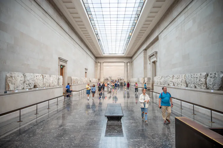 A large ceiling and well-lit room house walls lined with marble statues.