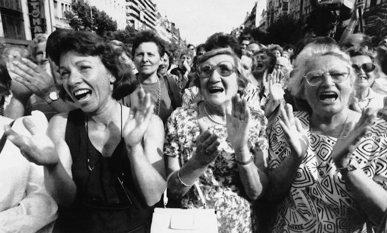 Una foto en blanco y negro muestra a tres mujeres en una multitud aplaudiendo y vitoreando.