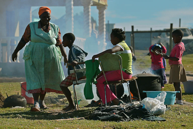 A woman and children cooking outdoors with firewood.