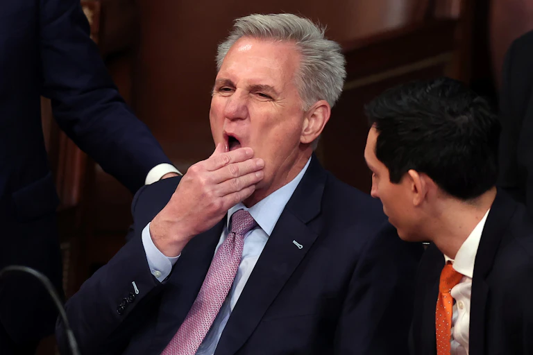 A man with gray hair in a suit strokes his chin in what appears to be a pained expression.