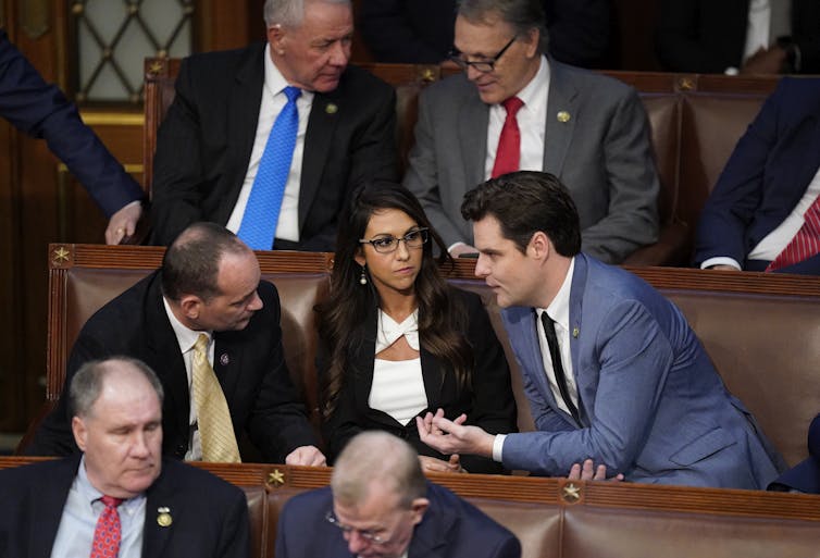 People chat while seated on brown benches.