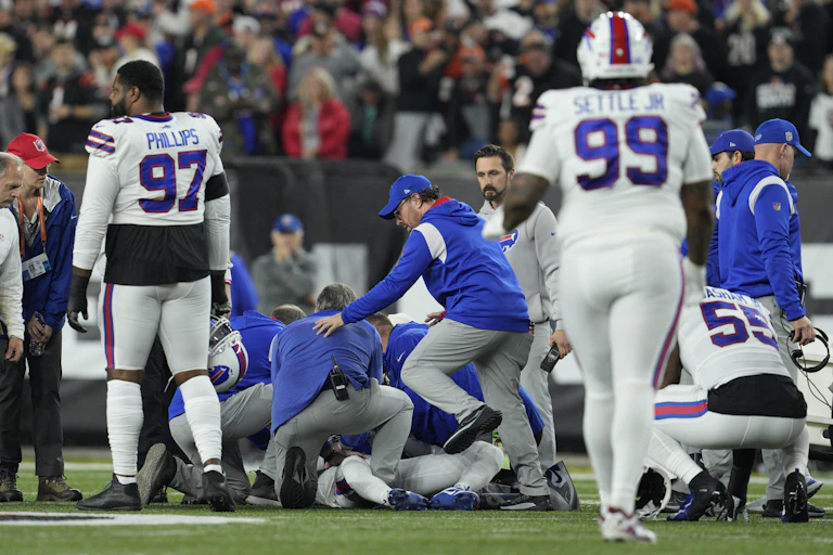 People in blue jackets and people in football uniforms crowd together on a field